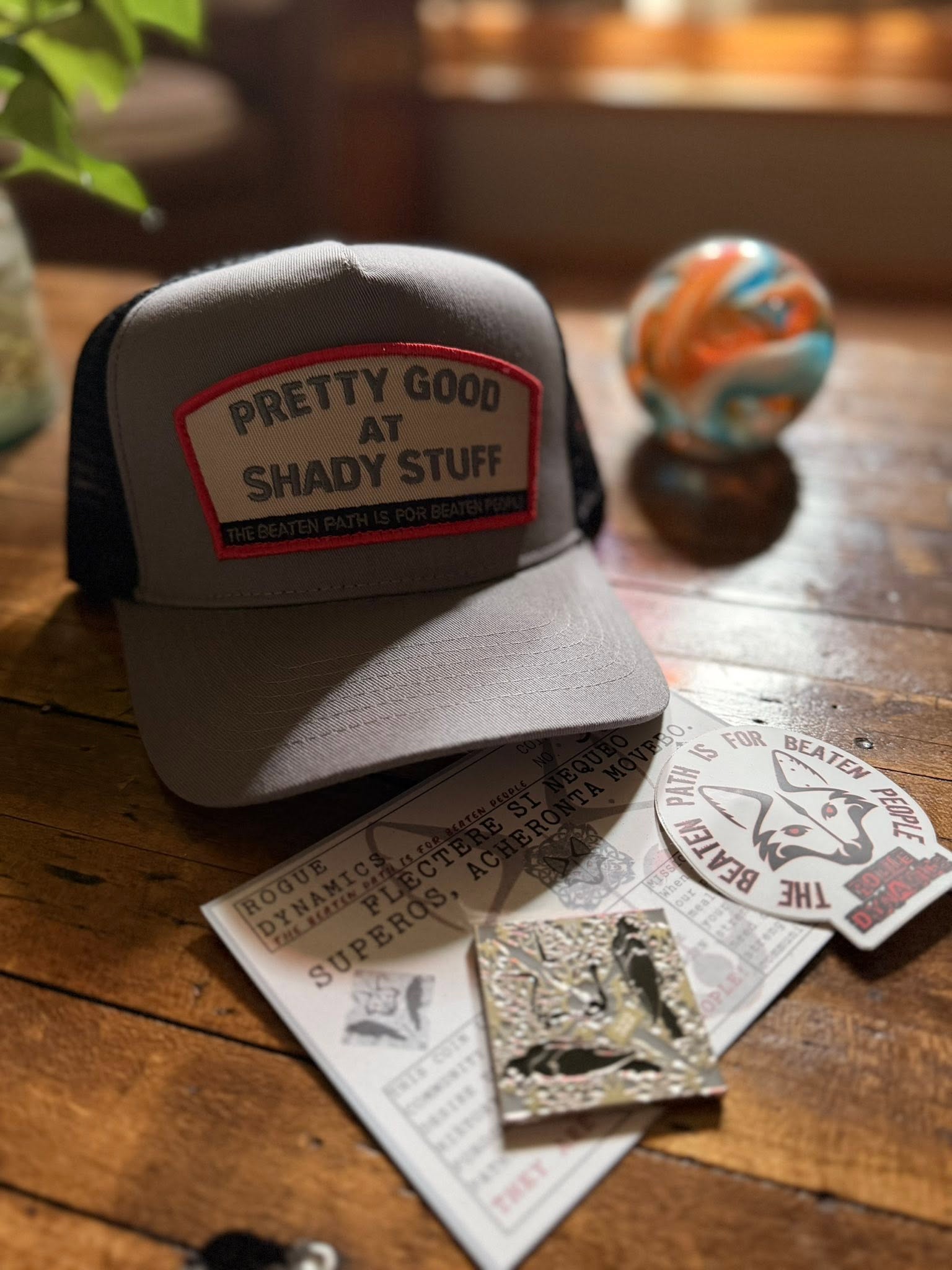 Shady Stuff hat with the Rogue Dynamics Labyrinth coin and stickers laid out beside it