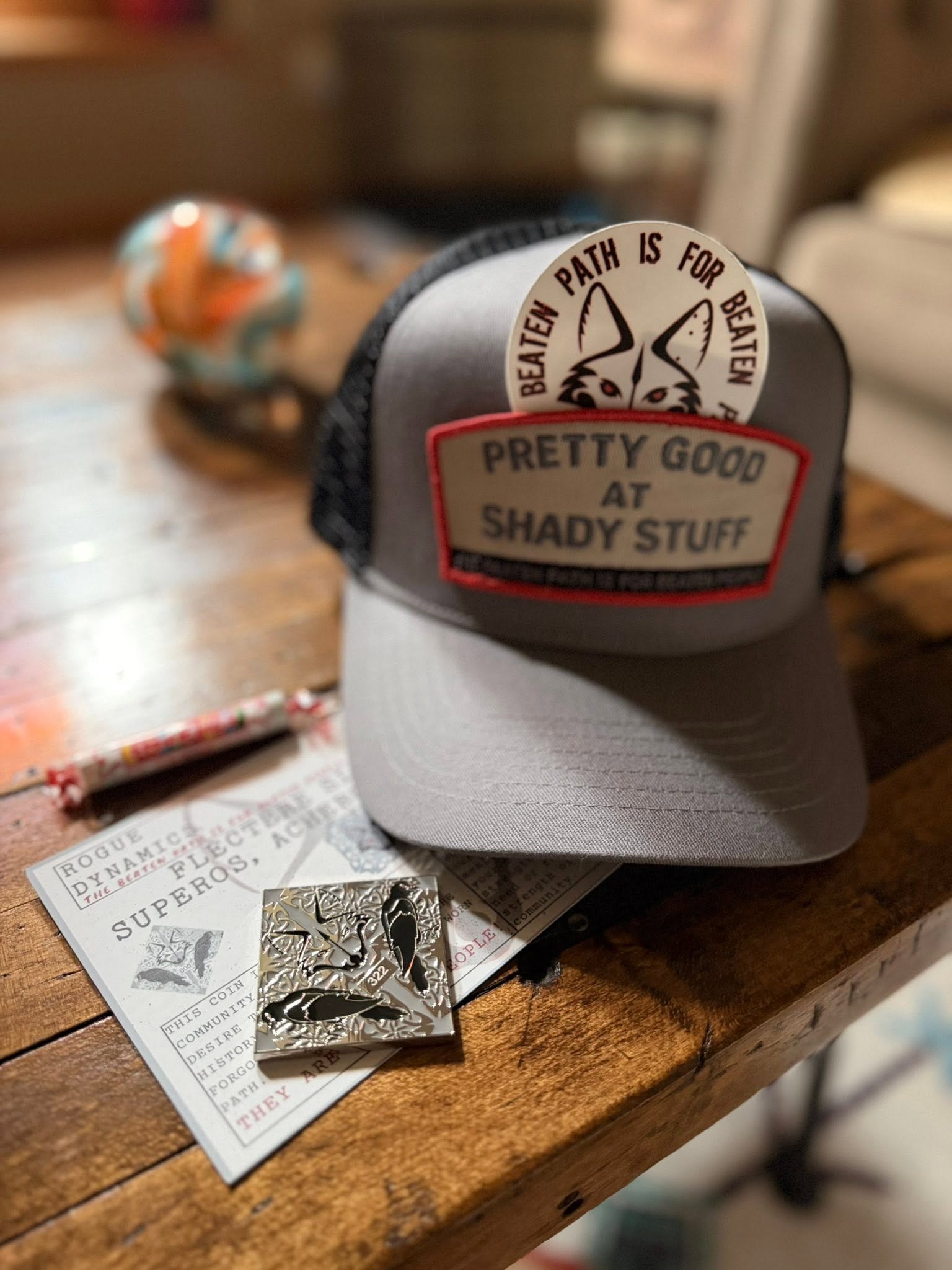 Shady Stuff hat, Labyrinth coin, and Rogue Dynamics fox sticker flatlay